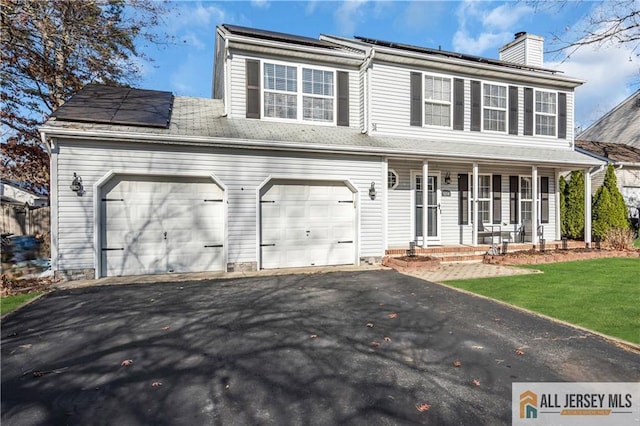 view of front facade with a garage, a front lawn, solar panels, and covered porch