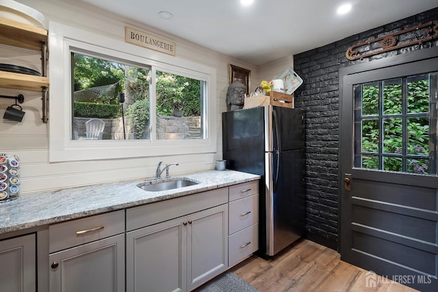 kitchen with light stone countertops, sink, stainless steel refrigerator, and light hardwood / wood-style flooring