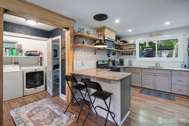 kitchen with kitchen peninsula, sink, washer and dryer, gray cabinets, and stainless steel range with gas cooktop