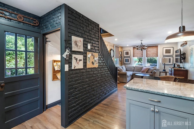 kitchen featuring light stone counters, brick wall, light hardwood / wood-style flooring, an inviting chandelier, and hanging light fixtures