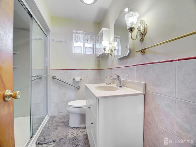 bathroom with tile walls, vanity, toilet, a stall shower, and a wainscoted wall