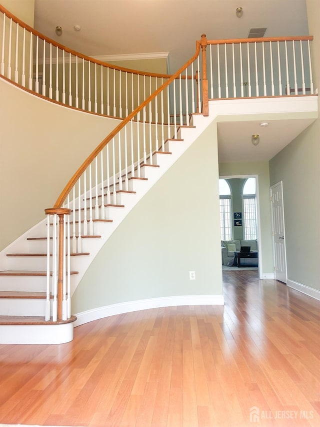 stairway featuring wood finished floors, baseboards, and a towering ceiling