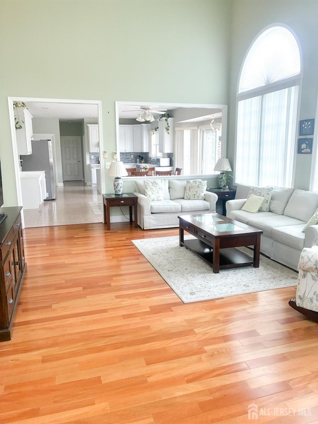 living room featuring a towering ceiling, light wood-type flooring, and baseboards