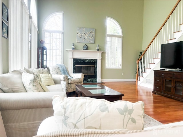 living room featuring stairway, wood finished floors, a fireplace, a towering ceiling, and baseboards