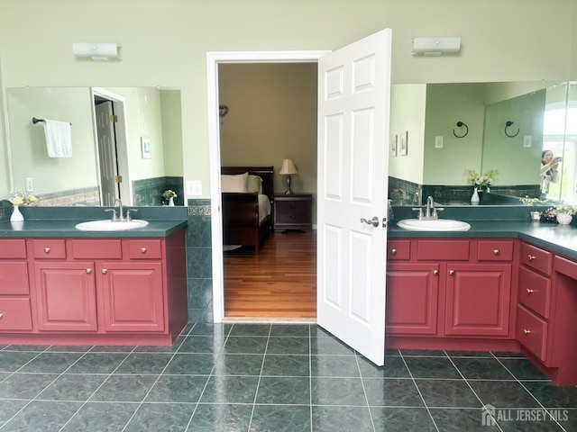 bathroom with tile patterned floors, ensuite bath, tile walls, a wainscoted wall, and two vanities