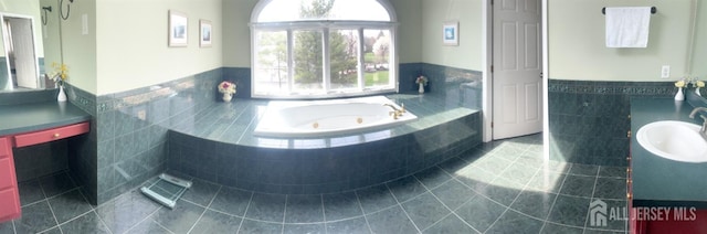 full bath with tile patterned floors, a tub with jets, tile walls, vanity, and wainscoting
