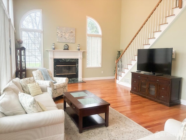living room featuring light wood finished floors, stairway, a towering ceiling, a high end fireplace, and baseboards