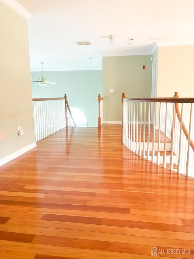 hall with an upstairs landing, wood finished floors, ornamental molding, and baseboards
