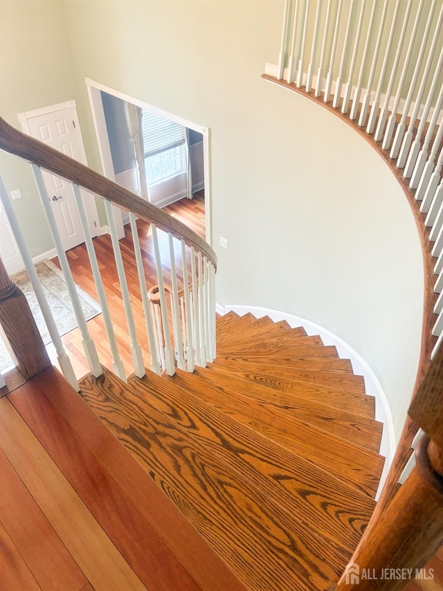 stairway with wood finished floors, a towering ceiling, and baseboards