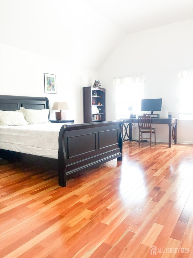 bedroom featuring light wood-style flooring, lofted ceiling, and a desk