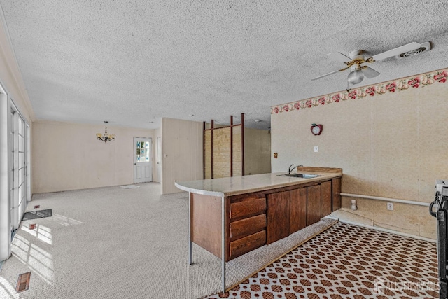 kitchen with ceiling fan with notable chandelier, kitchen peninsula, sink, and a textured ceiling