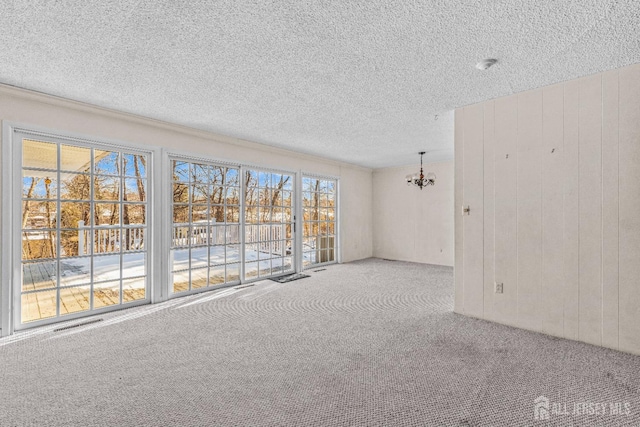 carpeted spare room with wooden walls, a textured ceiling, and a chandelier