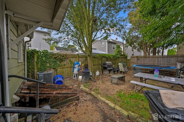 view of yard featuring a trampoline, a fenced backyard, and central AC unit