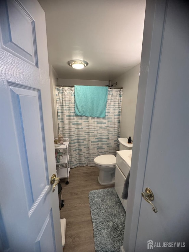 bathroom featuring a shower with shower curtain, toilet, wood finished floors, and vanity