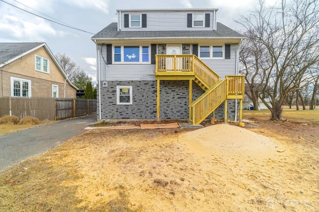 view of front facade featuring a shingled roof, fence, driveway, and stairs