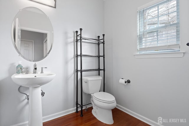 half bathroom with baseboards, toilet, and wood finished floors