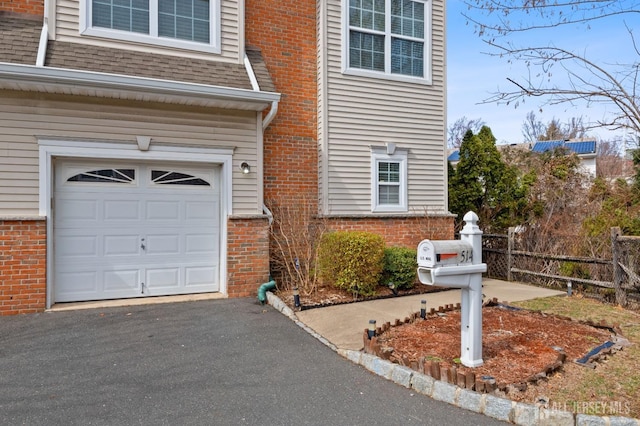 view of front facade featuring brick siding, fence, roof with shingles, a garage, and driveway