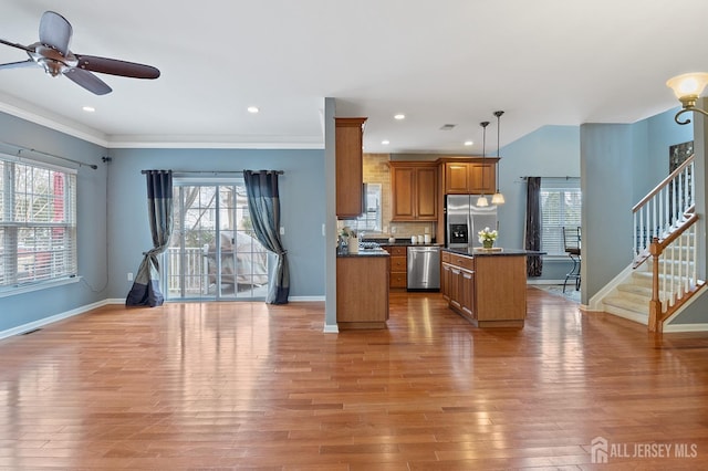 kitchen featuring brown cabinetry, light wood-style flooring, appliances with stainless steel finishes, dark countertops, and a center island