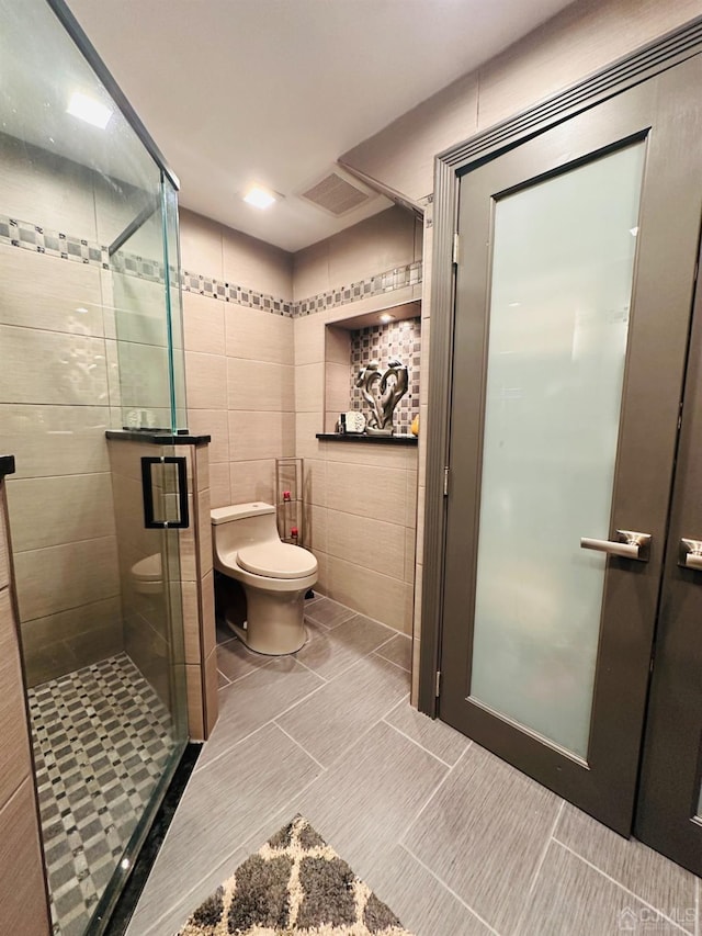 bathroom featuring toilet, a shower with door, and tile walls