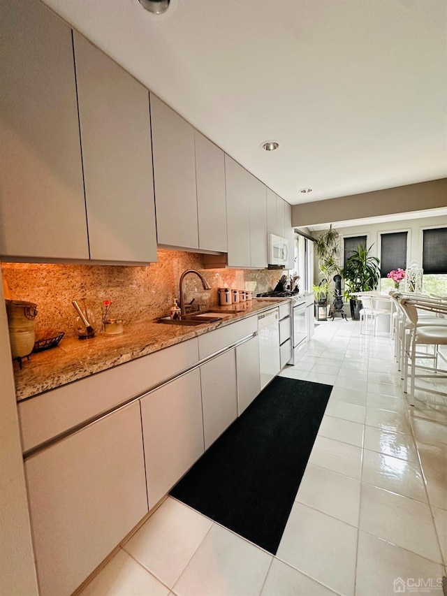 kitchen featuring light tile patterned flooring, tasteful backsplash, sink, light stone counters, and white appliances