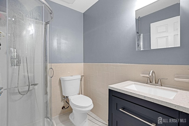 bathroom with tile walls, toilet, a shower stall, vanity, and a wainscoted wall