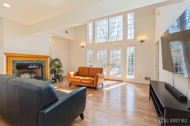 living room featuring visible vents, baseboards, a premium fireplace, french doors, and light wood-style floors