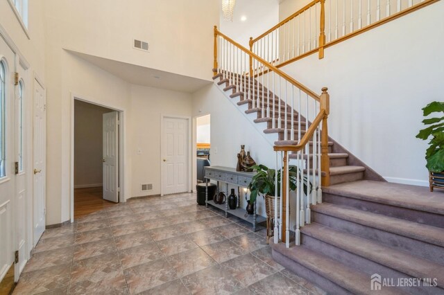 stairway featuring baseboards, visible vents, and a towering ceiling