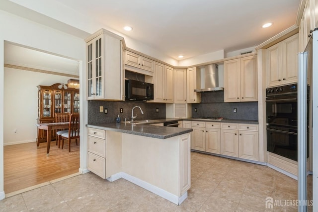 kitchen featuring dark countertops, a peninsula, black appliances, wall chimney exhaust hood, and a sink