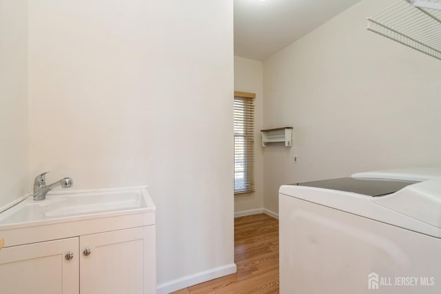 laundry area with baseboards, light wood finished floors, laundry area, a sink, and washer and dryer