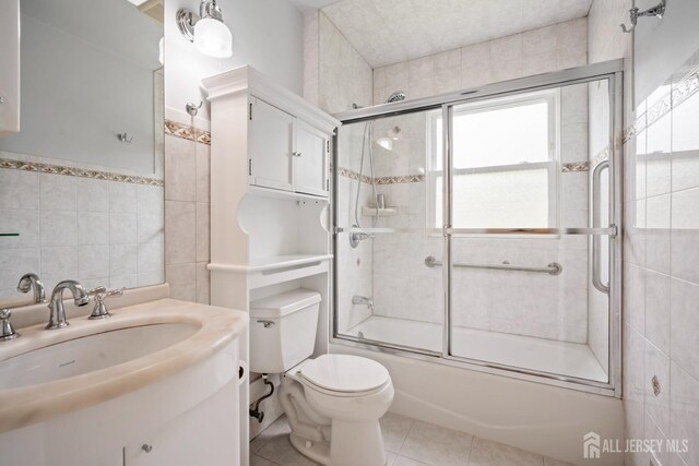 44 Frost Ave, East Brunswick, NJ 08816 - bathroom featuring combined bath / shower with glass door, toilet, vanity, tile walls, and tile patterned flooring