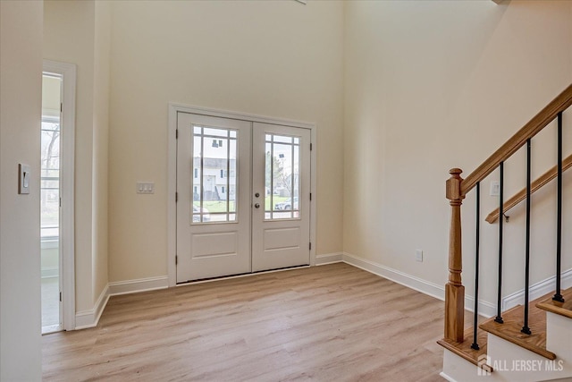 entrance foyer with light wood-type flooring, a towering ceiling, baseboards, and french doors