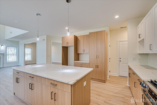 90 Hancock Rd, Piscataway, NJ 08854 - kitchen with stainless steel range with gas stovetop, light wood-style floors, light stone counters, a center island, and hanging light fixtures
