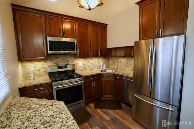 kitchen featuring tasteful backsplash, dark wood-style floors, appliances with stainless steel finishes, light stone counters, and a sink