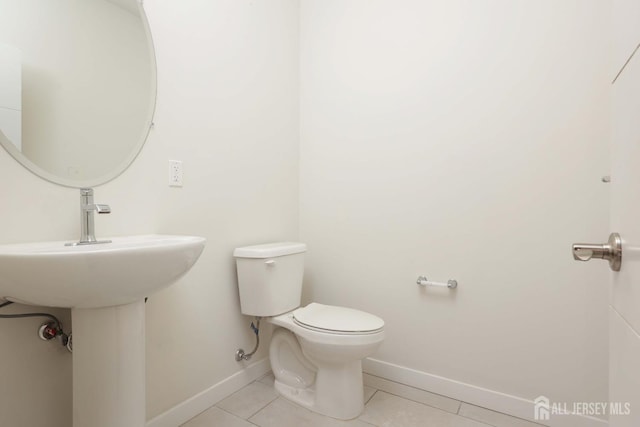 half bath featuring tile patterned flooring, toilet, and baseboards