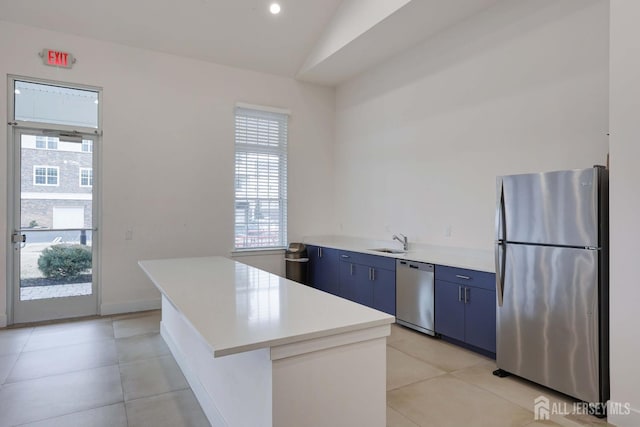 kitchen with blue cabinetry, light countertops, lofted ceiling, stainless steel appliances, and a sink