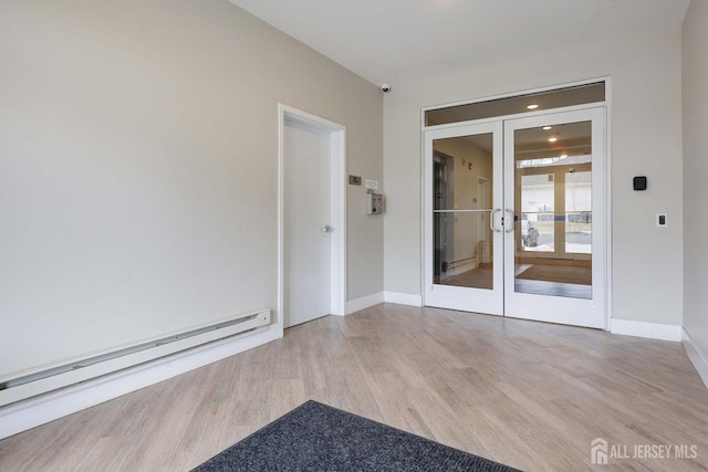 spare room featuring a baseboard heating unit, light wood-type flooring, french doors, and baseboards