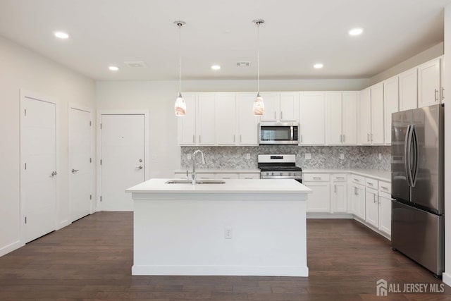 kitchen with a kitchen island with sink, a sink, backsplash, appliances with stainless steel finishes, and dark wood-style flooring