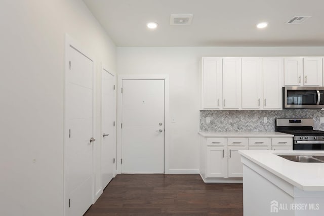 kitchen featuring visible vents, decorative backsplash, stainless steel appliances, white cabinetry, and dark wood-style flooring