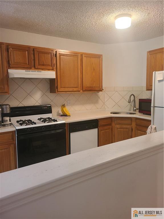 297 Prestwick Way Unit 297, Edison, NJ 08820 - kitchen featuring white appliances, under cabinet range hood, a sink, light countertops, and decorative backsplash