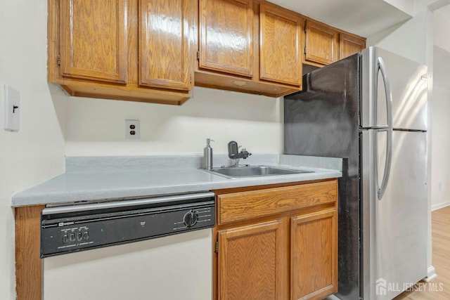 kitchen featuring brown cabinets, a sink, freestanding refrigerator, white dishwasher, and light countertops