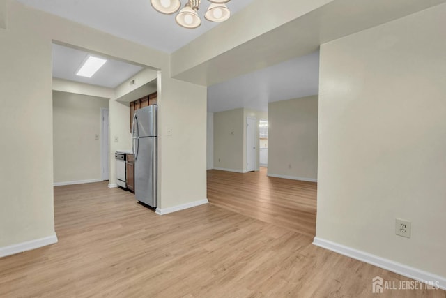 spare room with a notable chandelier, baseboards, and light wood-style floors