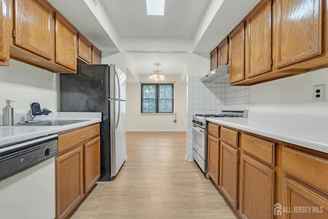 kitchen with under cabinet range hood, stainless steel appliances, decorative backsplash, and brown cabinetry