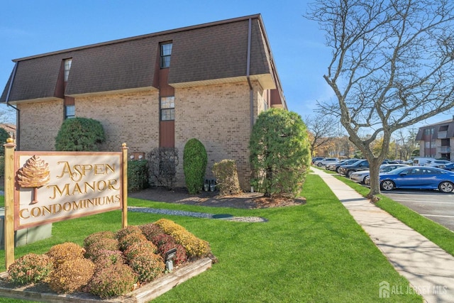 community / neighborhood sign featuring a lawn and uncovered parking