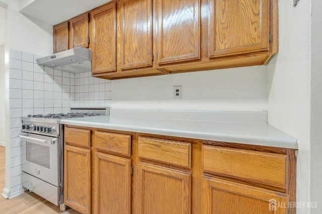 kitchen with high end stove, decorative backsplash, light countertops, light wood-style floors, and under cabinet range hood