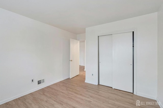 unfurnished bedroom featuring light wood finished floors, visible vents, a closet, and baseboards