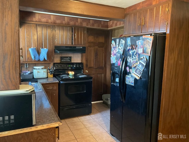 kitchen featuring light tile patterned floors, decorative backsplash, wooden walls, and black appliances