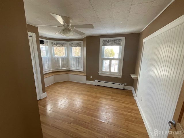 empty room featuring ceiling fan, crown molding, baseboard heating, and light hardwood / wood-style floors