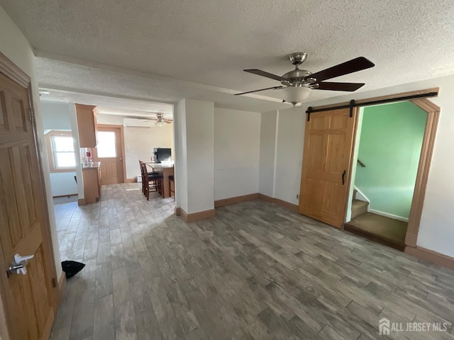 unfurnished bedroom with a barn door, hardwood / wood-style floors, a textured ceiling, and an AC wall unit