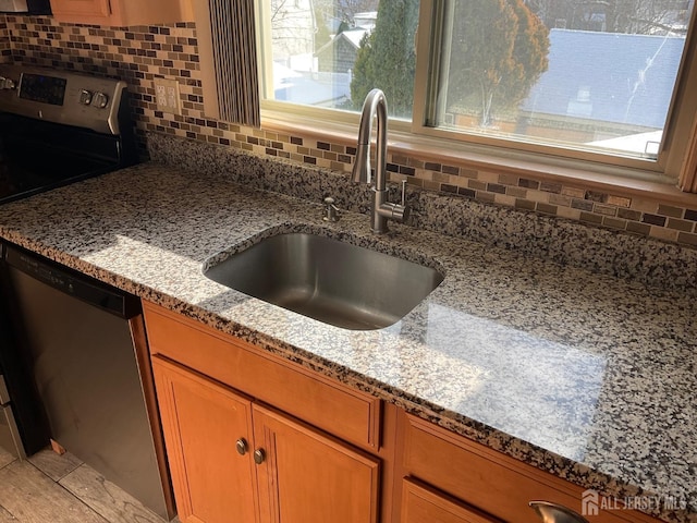 kitchen featuring light stone countertops, sink, stainless steel dishwasher, and decorative backsplash