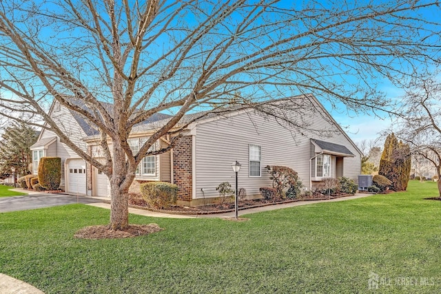 view of side of home featuring brick siding, a lawn, an attached garage, central AC unit, and driveway